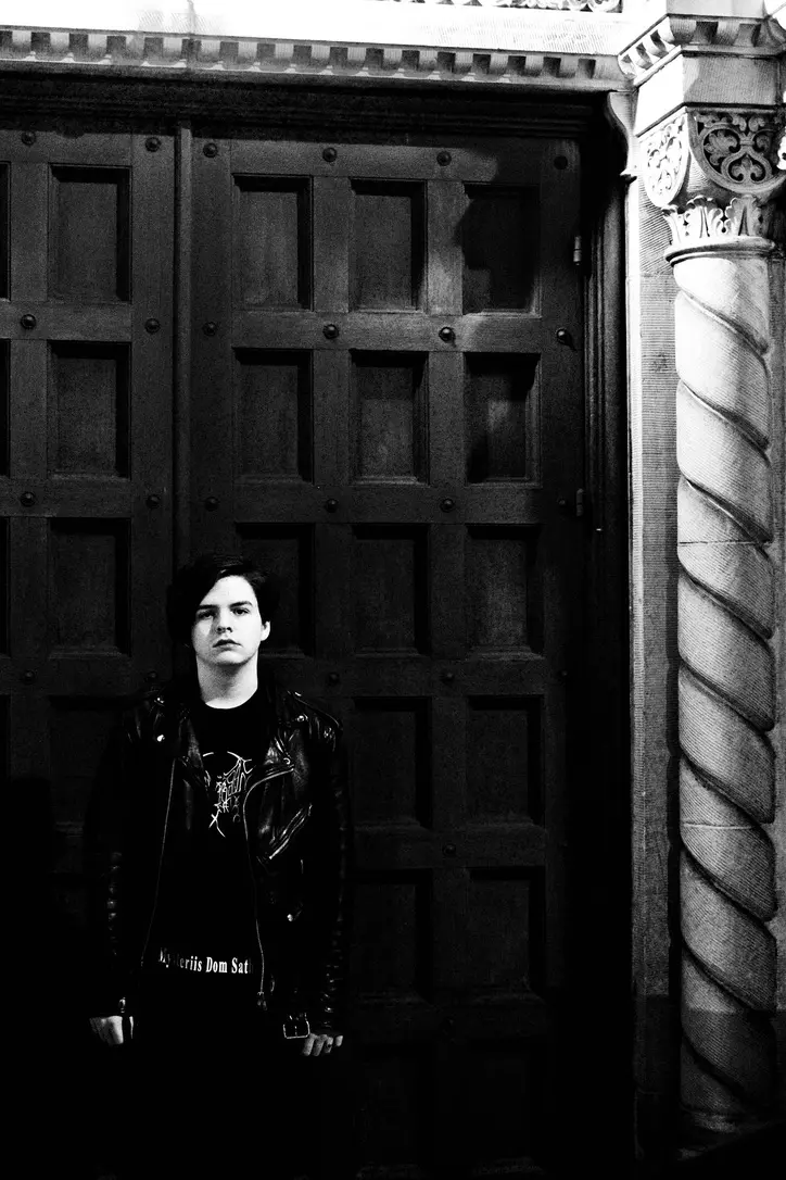 A photograph of the extreme metal musician, Miles Plumb, wearing a leather jacket and Mayhem shirt in front of a church in Koreatown, Los Angeles.